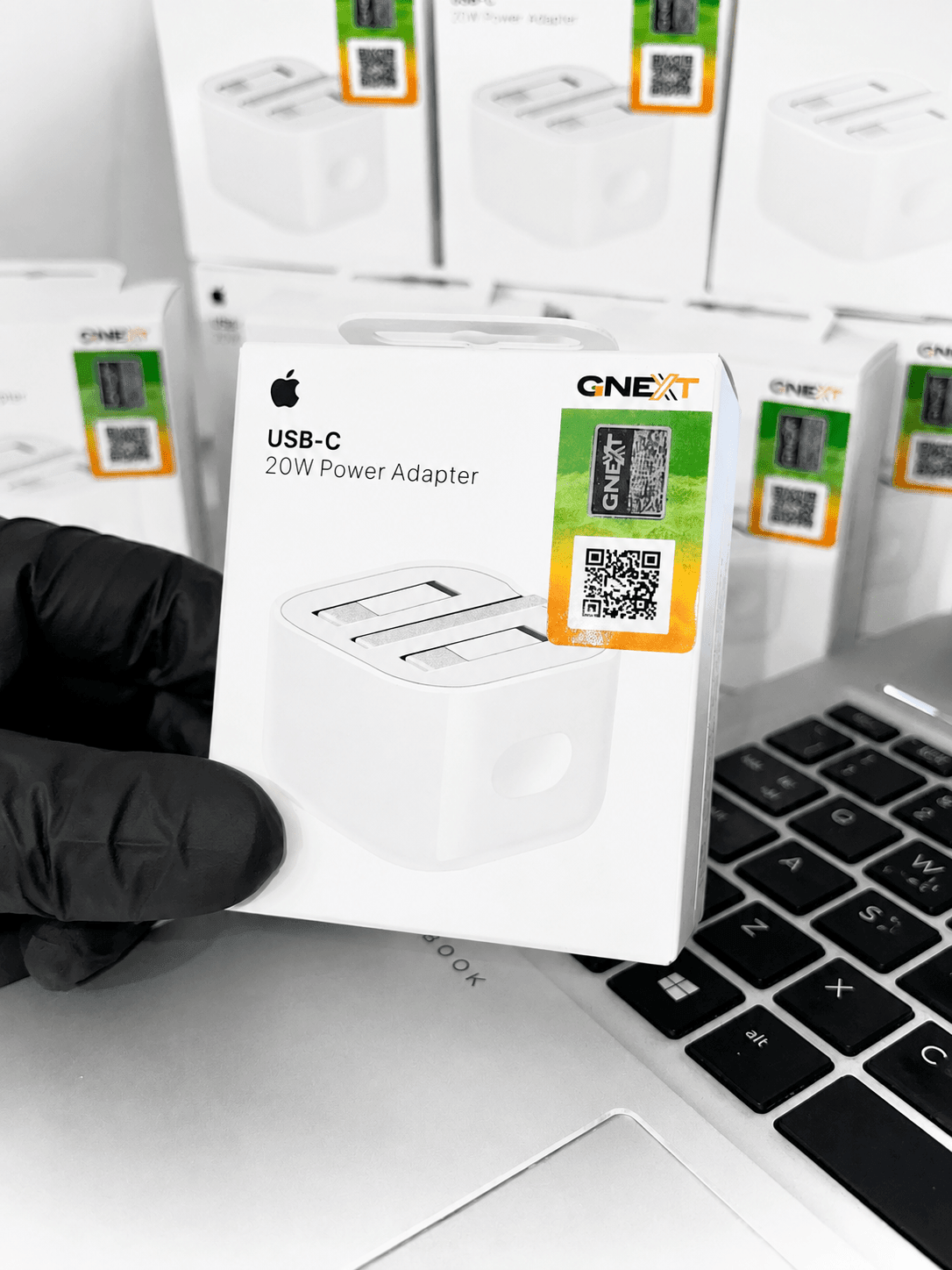 Apple USB-C 20W Power Adapter in retail packaging held over a laptop keyboard.