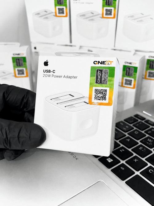 Apple USB-C 20W Power Adapter in retail packaging held over a laptop keyboard.