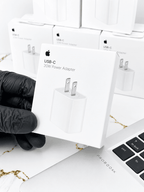 Hand holding an Apple USB-C 20W Power Adapter box against a background of multiple adapter boxes.