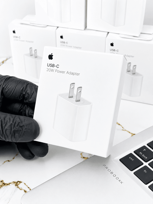 Hand holding an Apple USB-C 20W Power Adapter box against a background of multiple adapter boxes.