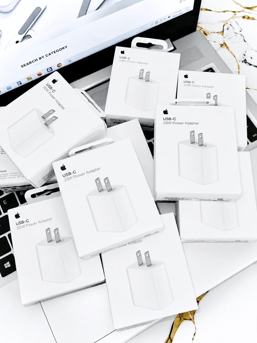 Multiple boxed USB-C 20W Power Adapters scattered on a laptop surface.