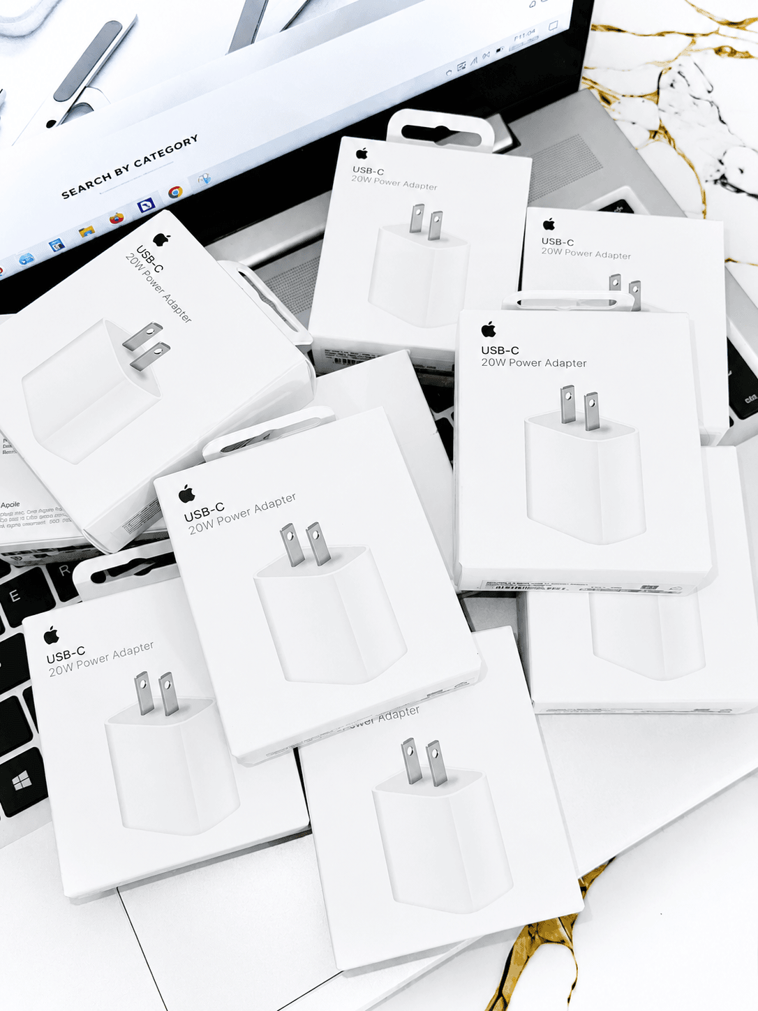 Multiple boxed USB-C 20W Power Adapters scattered on a laptop surface.