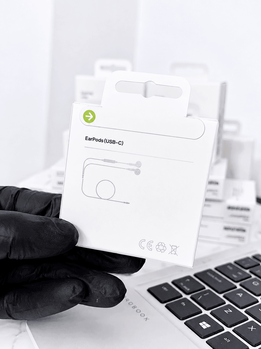 Hand in black glove holding EarPods (USB-C) packaging next to a laptop keyboard