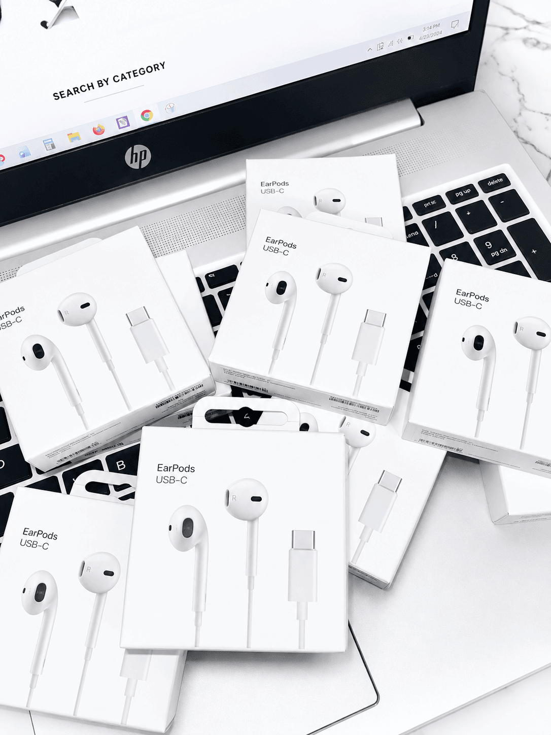 Multiple boxes of Apple EarPods USB-C headphones placed on a laptop keyboard.
