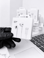 A hand in a black glove holding a box of USB-C EarPods next to a laptop.