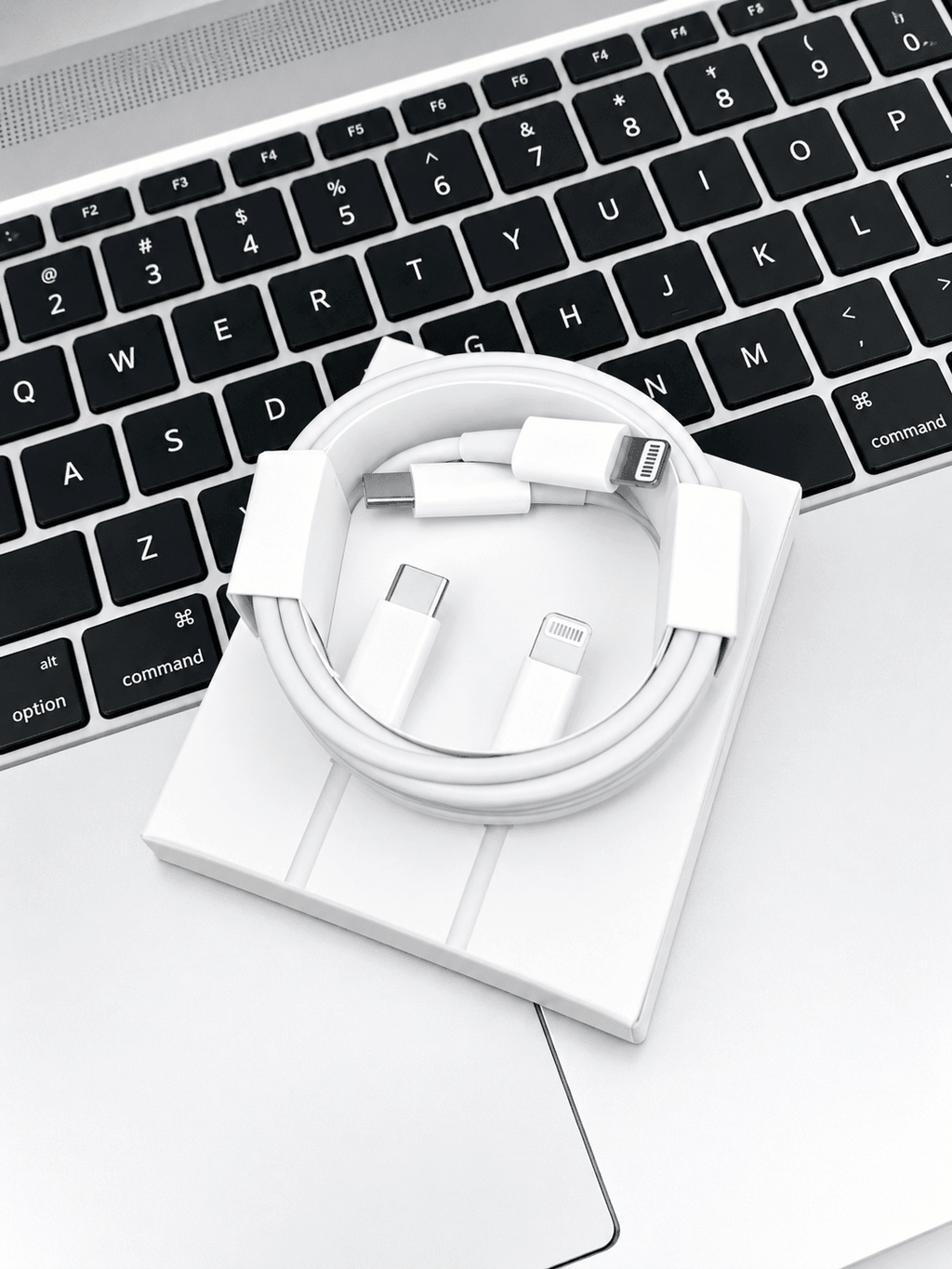 Coiled white USB-C to Lightning charging cable resting on a laptop keyboard